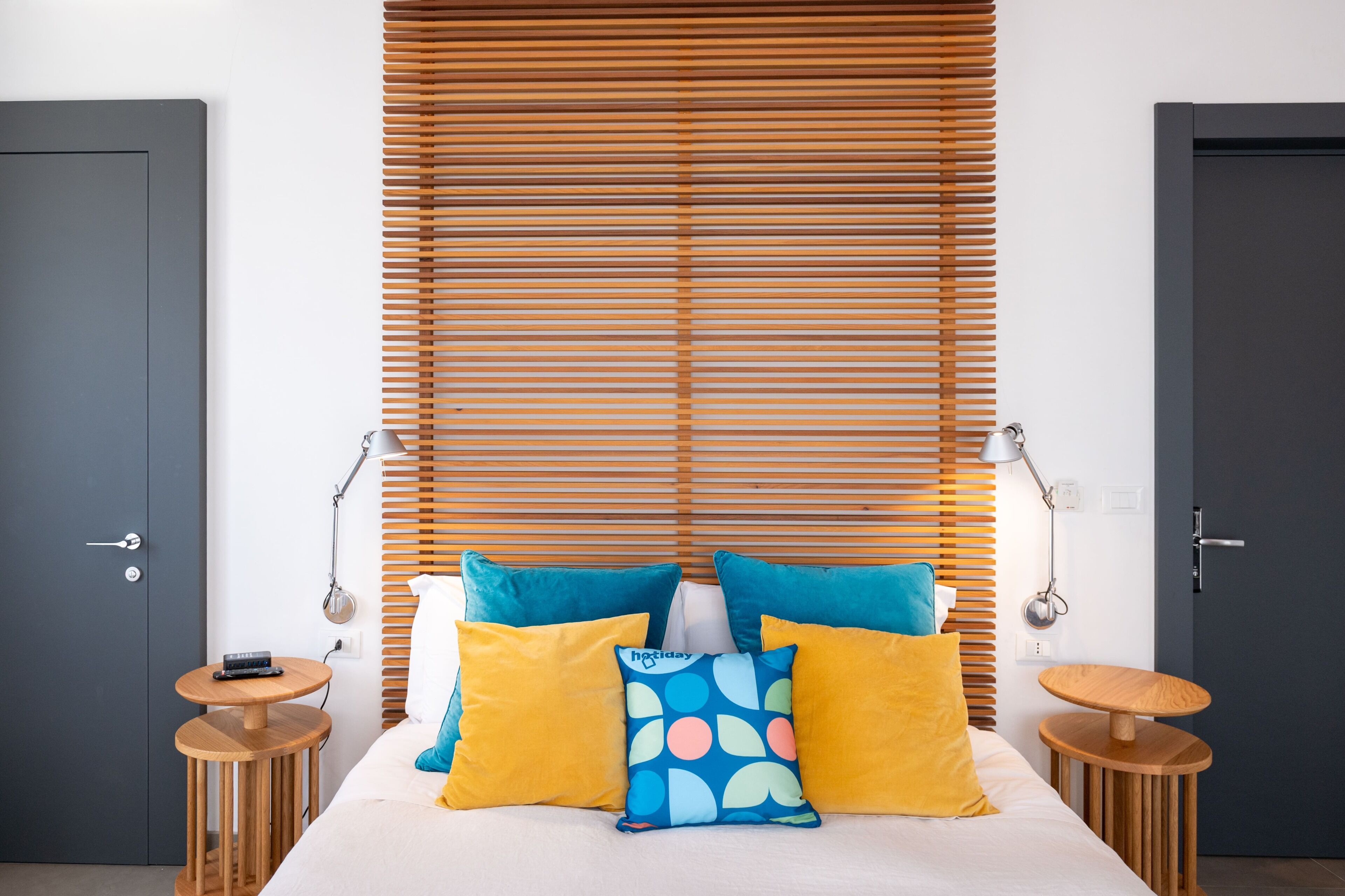 Une chambre à coucher avec un lit, des stores en bois, une table de chevet, une lampe et une porte.