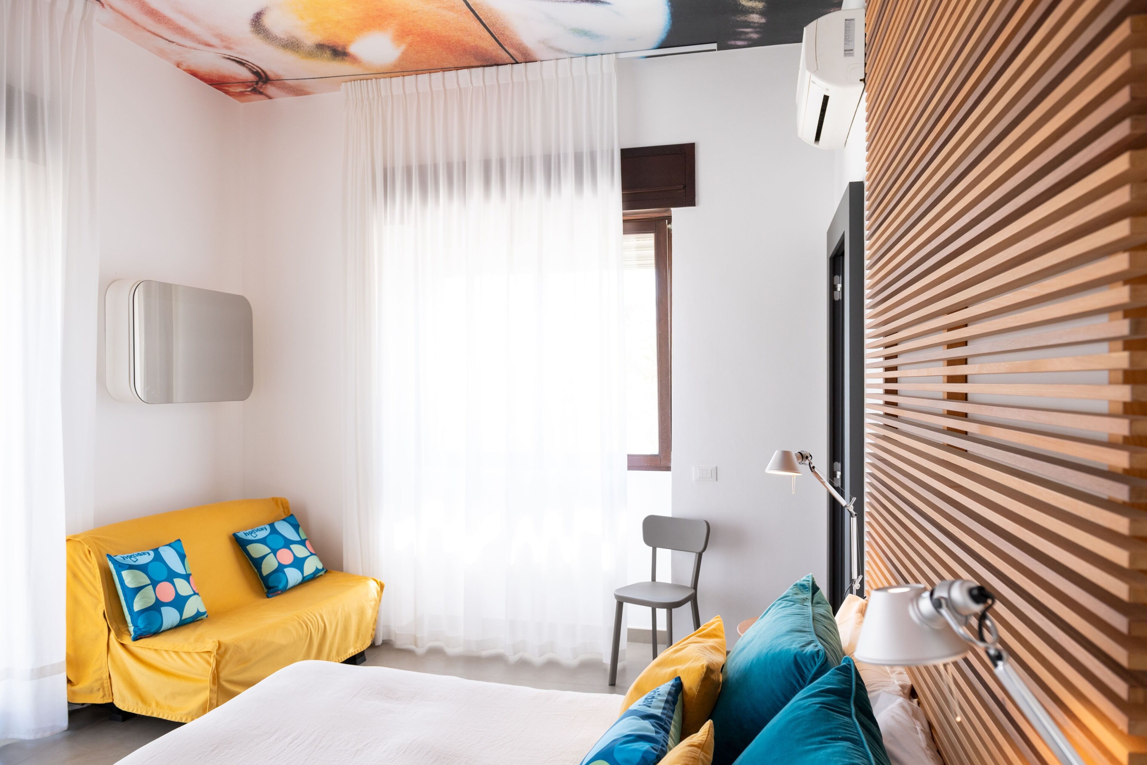 A modern hotel room with a bed, a sofa, a chair, and a wooden slatted wall.