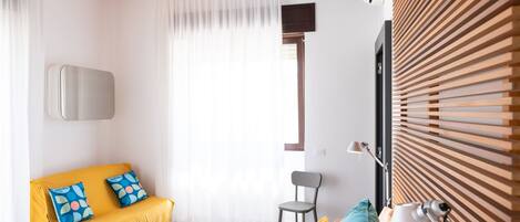 A modern hotel room with a bed, a sofa, a chair, and a wooden slatted wall.