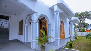 A white building with arched doorways, wooden doors, and a small garden area with potted plants. - No 36 Mirissa (Mirissa)