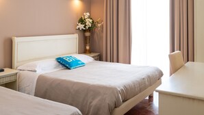 Een hotelkamer met twee bedden, een bureau, een vaas met bloemen en een groot raam met gordijnen.