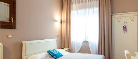 A hotel room with a bed, a nightstand, a desk, a wardrobe, and a window with curtains.