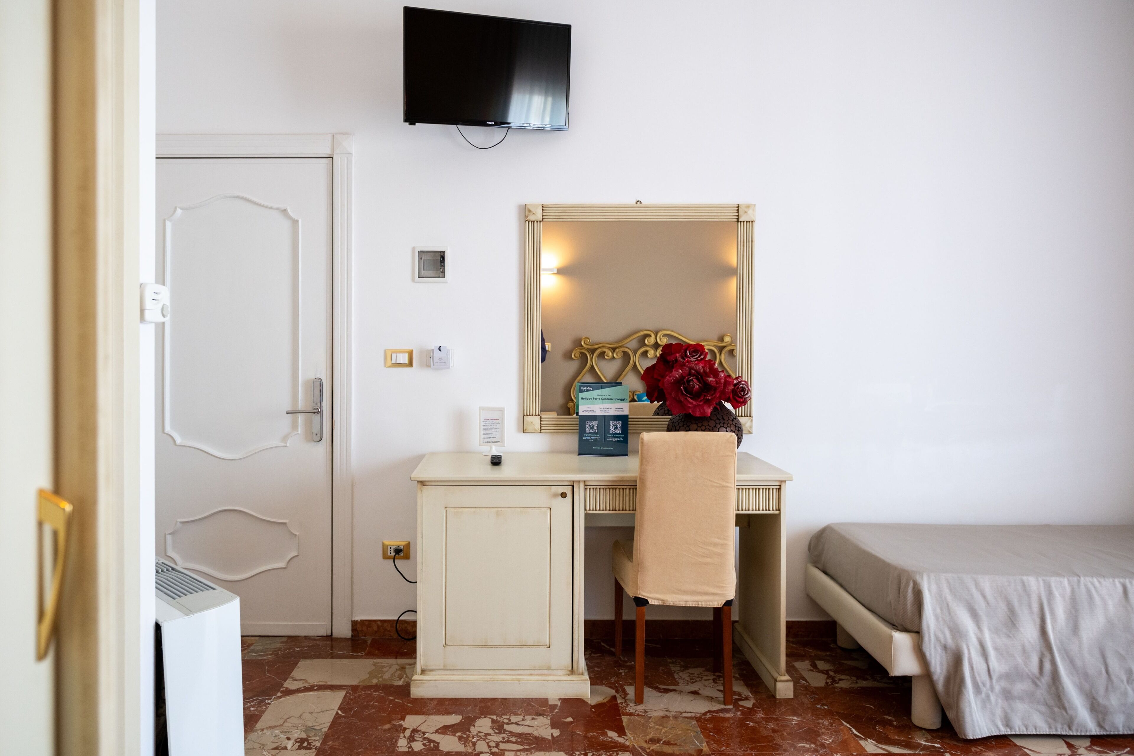 A room with a bed, a desk with a chair, a television, a mirror, and a door.