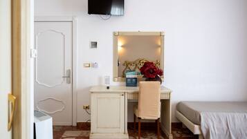 A room with a bed, a desk with a chair, a television, a mirror, and a door.