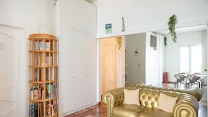 Een woonkamer met een gouden leren bank, een houten boekenkast en een witte kledingkast.