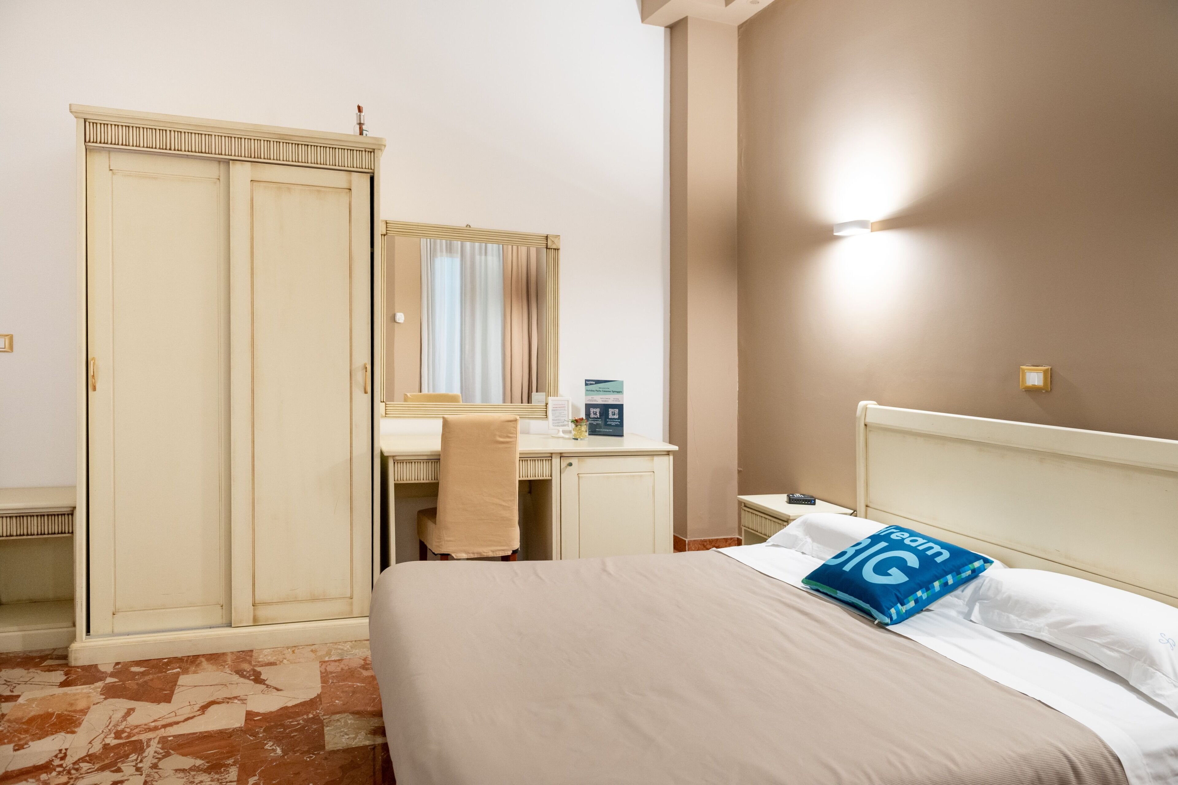 Une chambre d’hôtel comprenant un lit, un bureau, une armoire et un miroir.