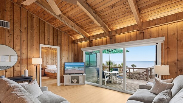 Un intérieur en bois avec une télévision, un canapé et un balcon offrant une vue sur la mer.