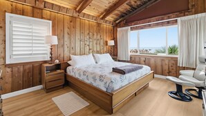 Une chambre à coucher aux murs lambrissés, avec un lit, des tables de chevet et une fenêtre avec des rideaux.