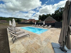 A swimming pool with lounge chairs and umbrellas, surrounded by a stone deck and a stone wall.