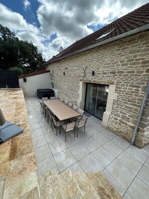 An outdoor patio with a stone wall, a large wooden table, and chairs.