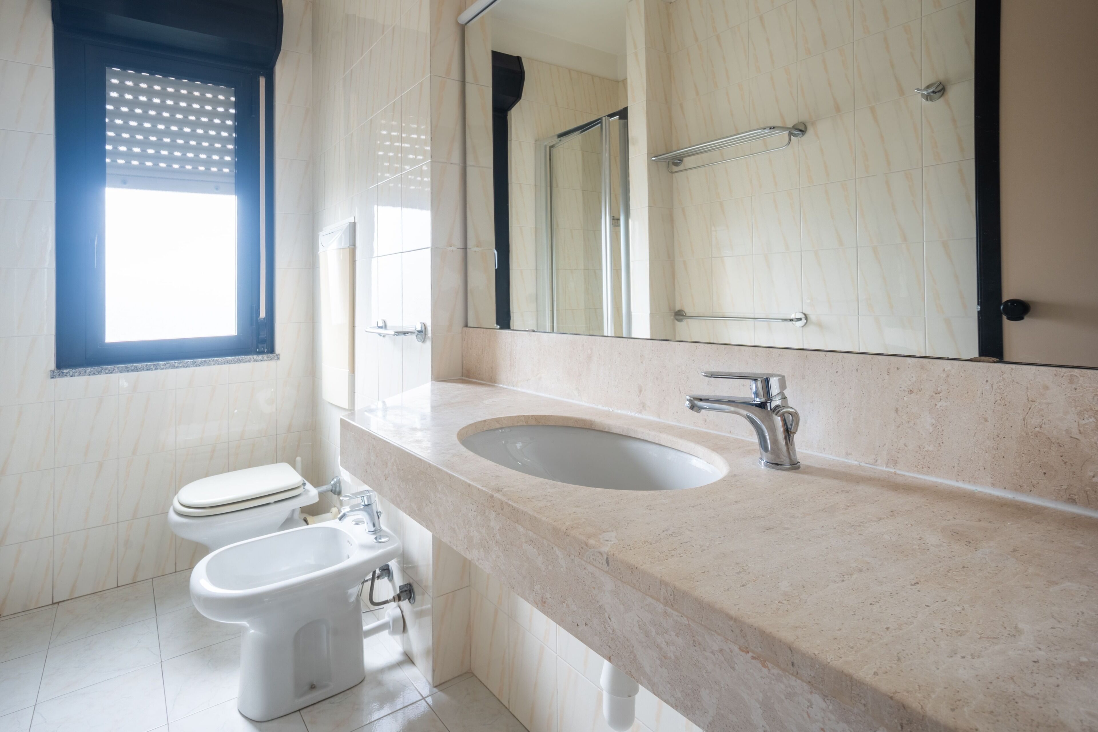 A bathroom with a toilet, bidet, sink, and a large mirror.