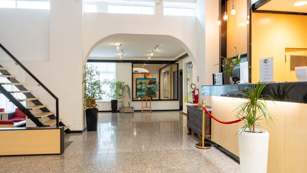 A hotel lobby with a staircase, reception desk, and artwork. - Hotiday Cagliari Sant'Elena (Quartu Sant'Elena)