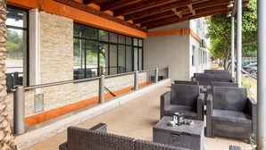 An outdoor patio with wicker furniture, a stone wall, and a view of the street. - Hotiday Cagliari Sant'Elena (Quartu Sant'Elena)