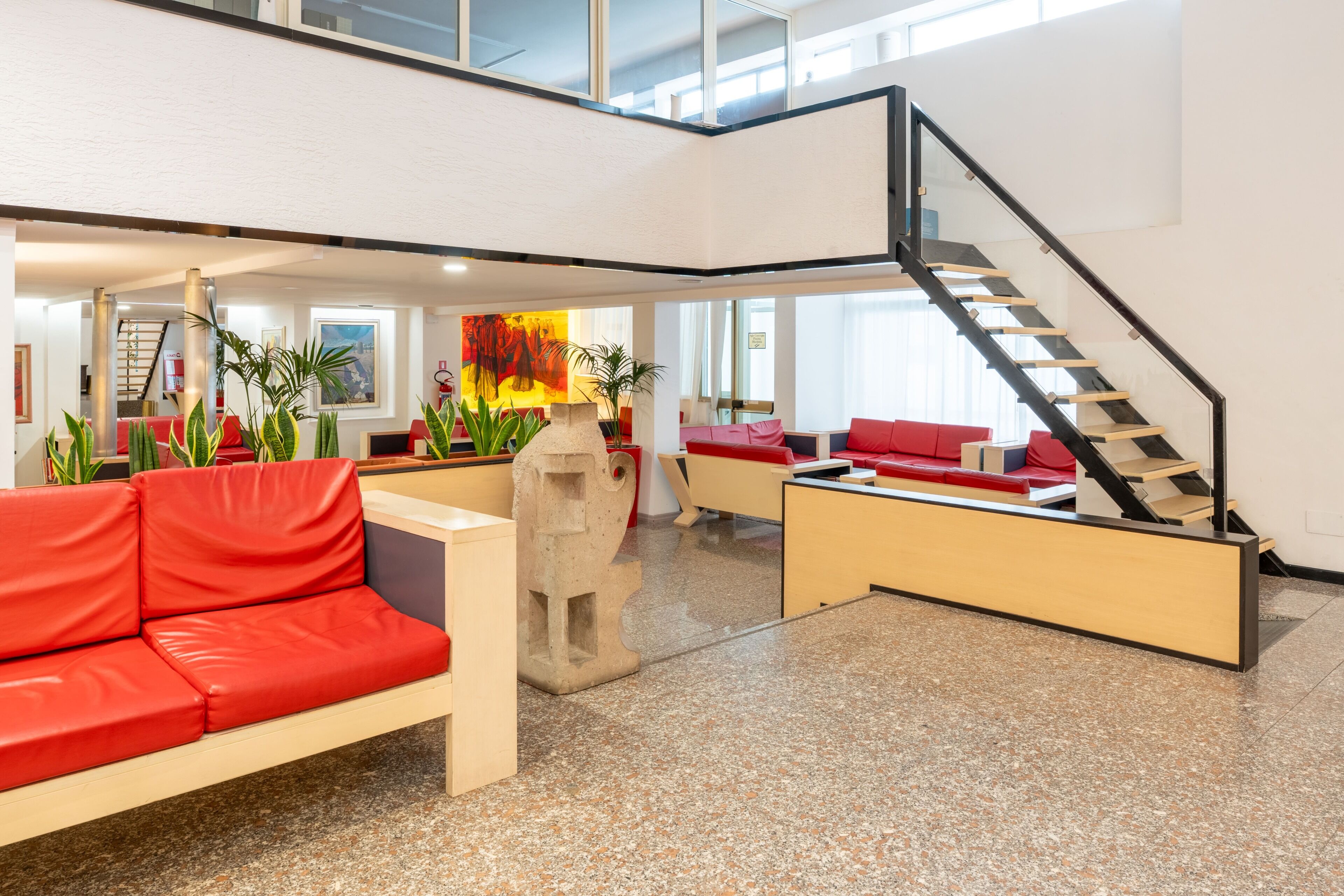 A spacious lobby with a red sofa, a staircase, and a large abstract painting.