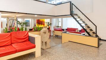 A spacious lobby with a red sofa, a staircase, and a large abstract painting.