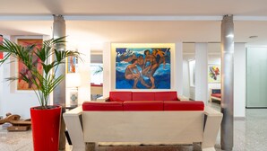 A modern lobby with a red sofa, a large painting, and a tall red planter. - Hotiday Cagliari Sant'Elena (Quartu Sant'Elena)
