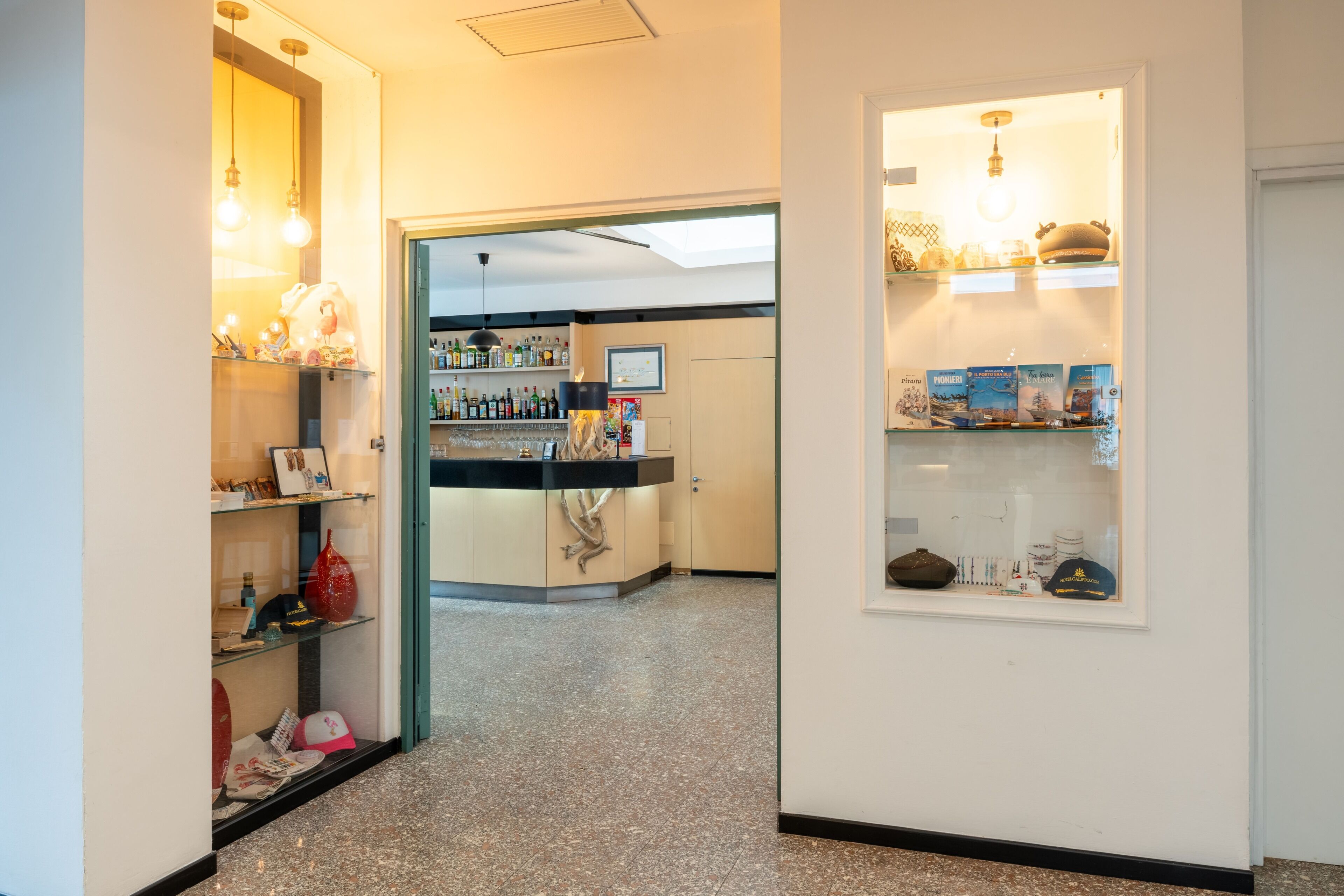 Un pasillo con un mostrador de recepción, una vitrina de vidrio con varios artículos y un mostrador con estantes llenos de botellas.
