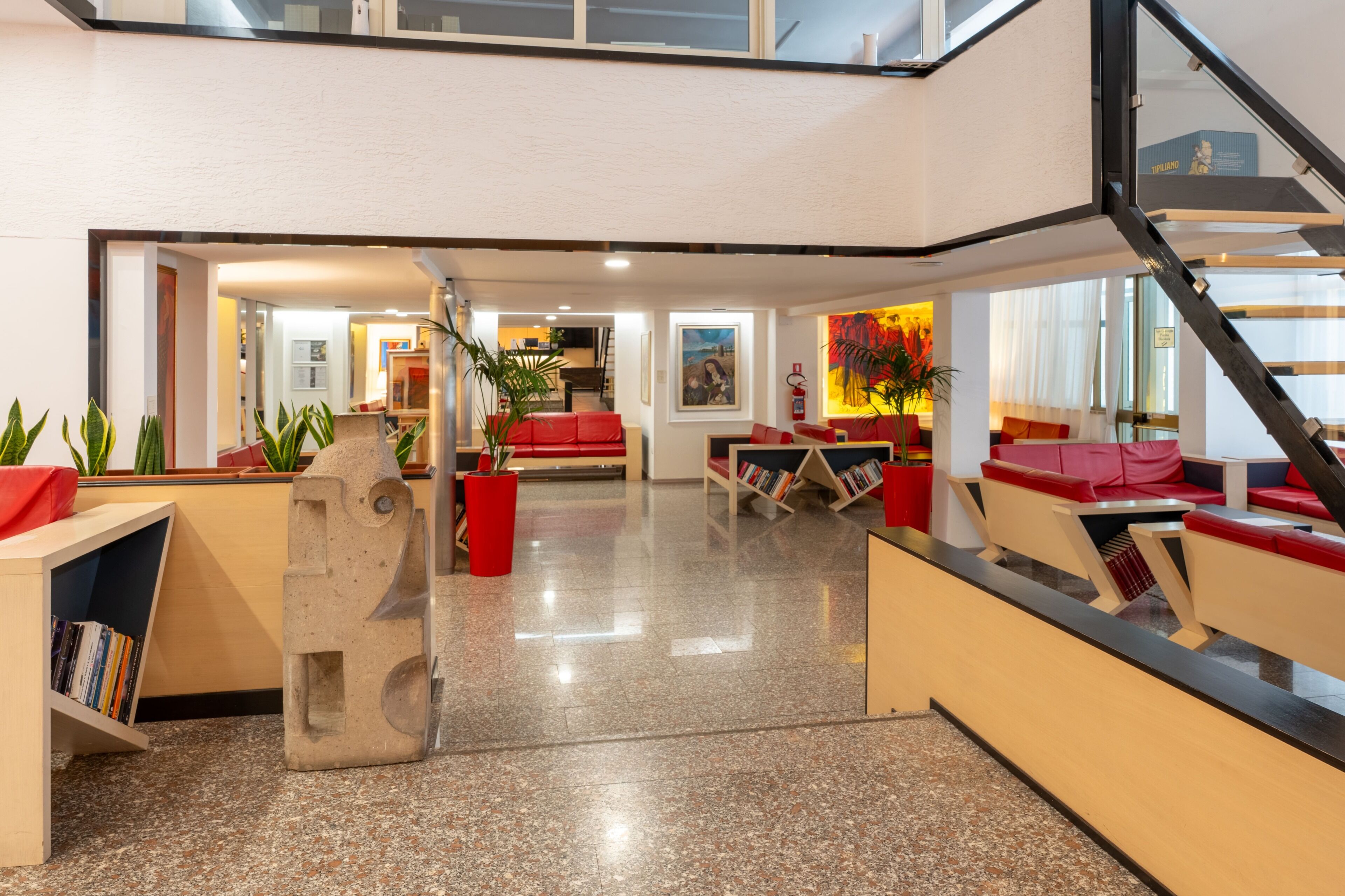 Un moderno vestíbulo de hotel con una escalera, zonas de estar y un mostrador de recepción.