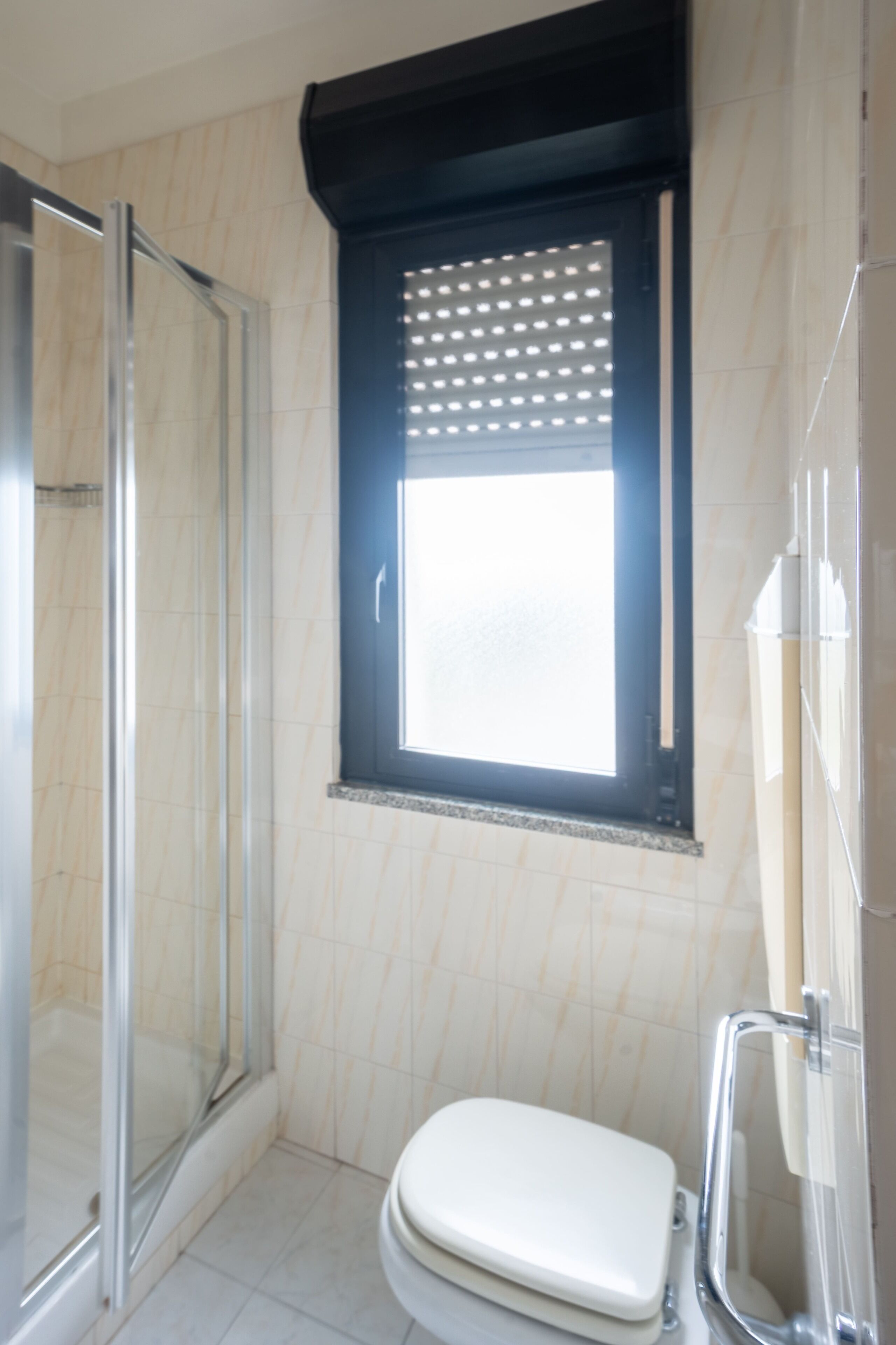 Un baño con inodoro, cabina de ducha y una ventana con persianas.