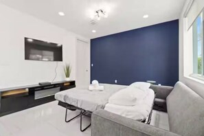 Ein modernes Zimmer mit grauem Sofa, einem kleinen Tisch und einem wandmontierten Flachbildfernseher.