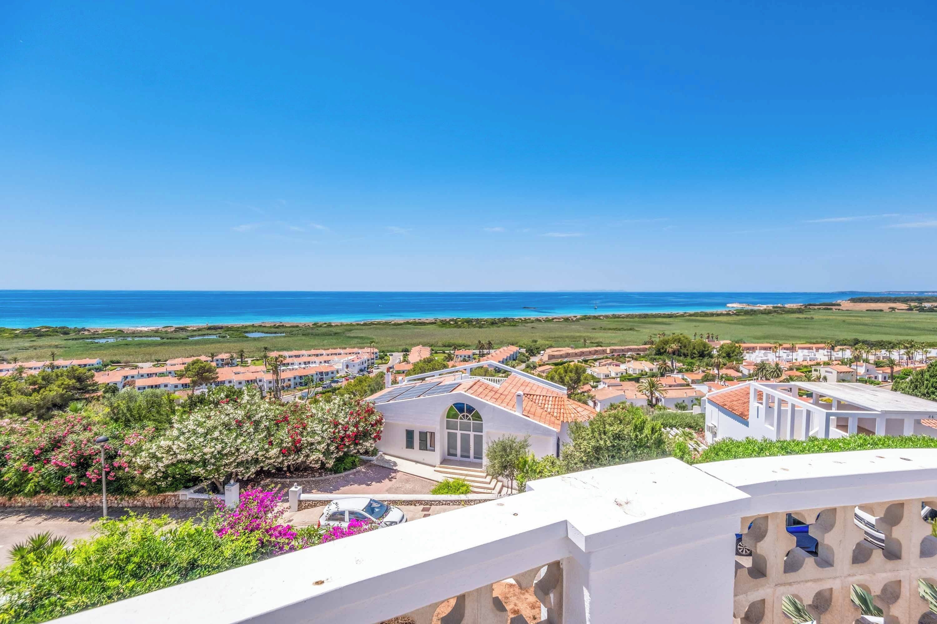 A coastal residential area with houses, a clear blue sky, and a view of the sea.