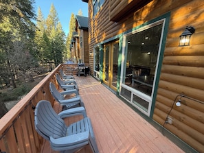 A wooden deck with outdoor seating and a view of the forest. - Sierra Chalet has 6 bedrooms, 4 full bathrooms, and 13 beds and driveway. (Shaver Lake)