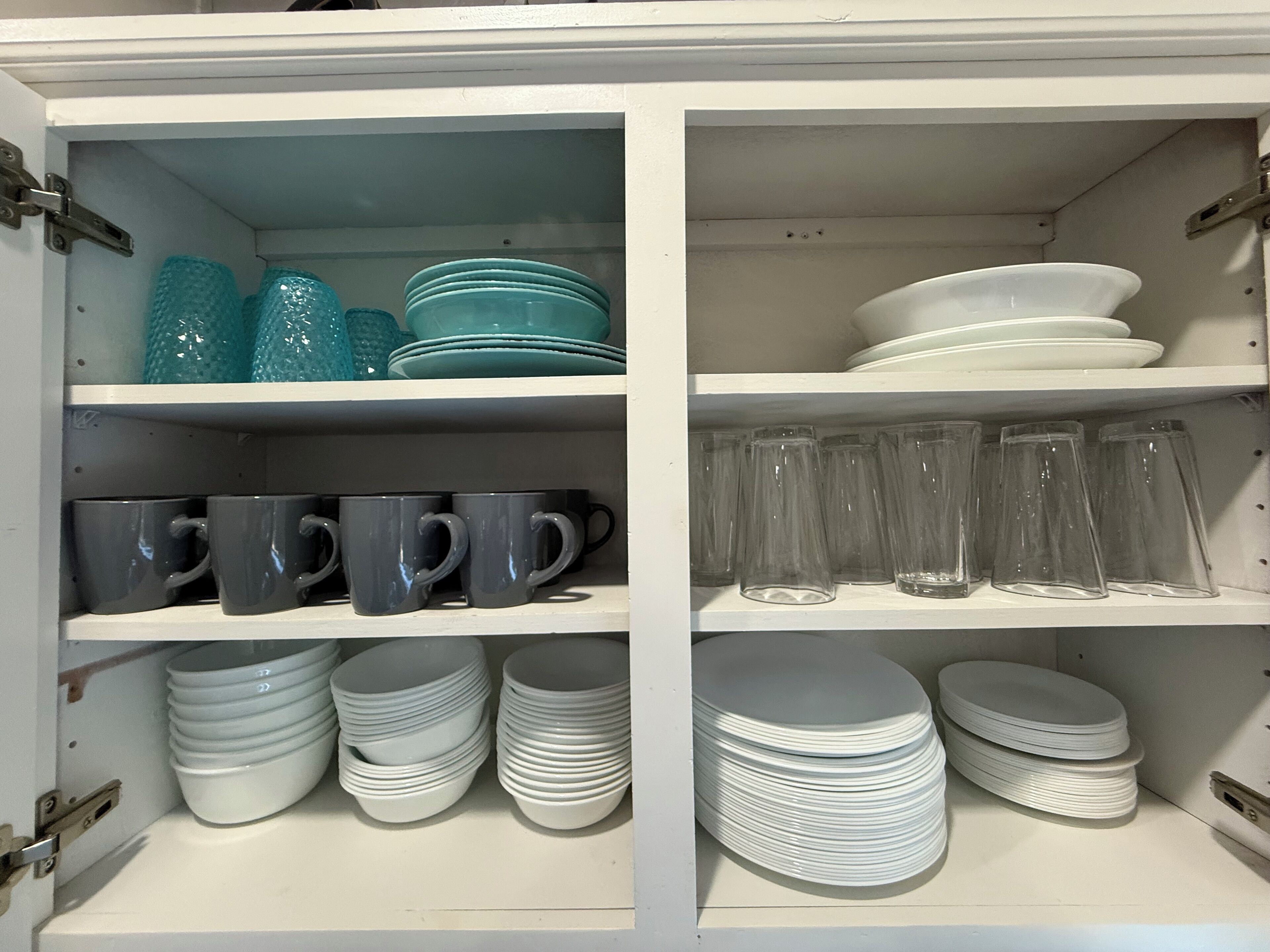 A cabinet with shelves containing stacks of white plates, blue glass bowls, and clear glass cups.