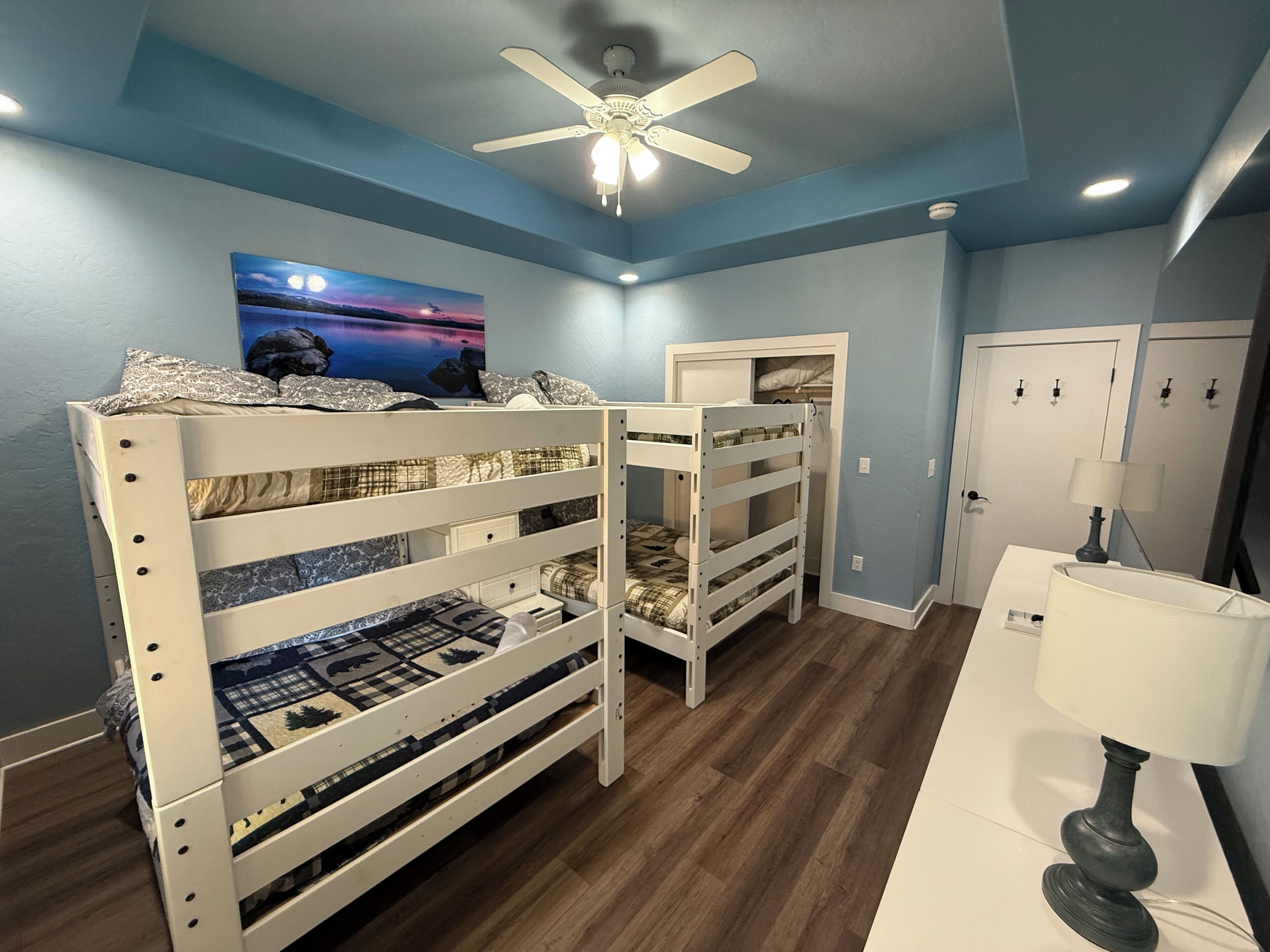 Une pièce avec des lits superposés, un ventilateur de plafond, un tableau, une porte et une lampe.