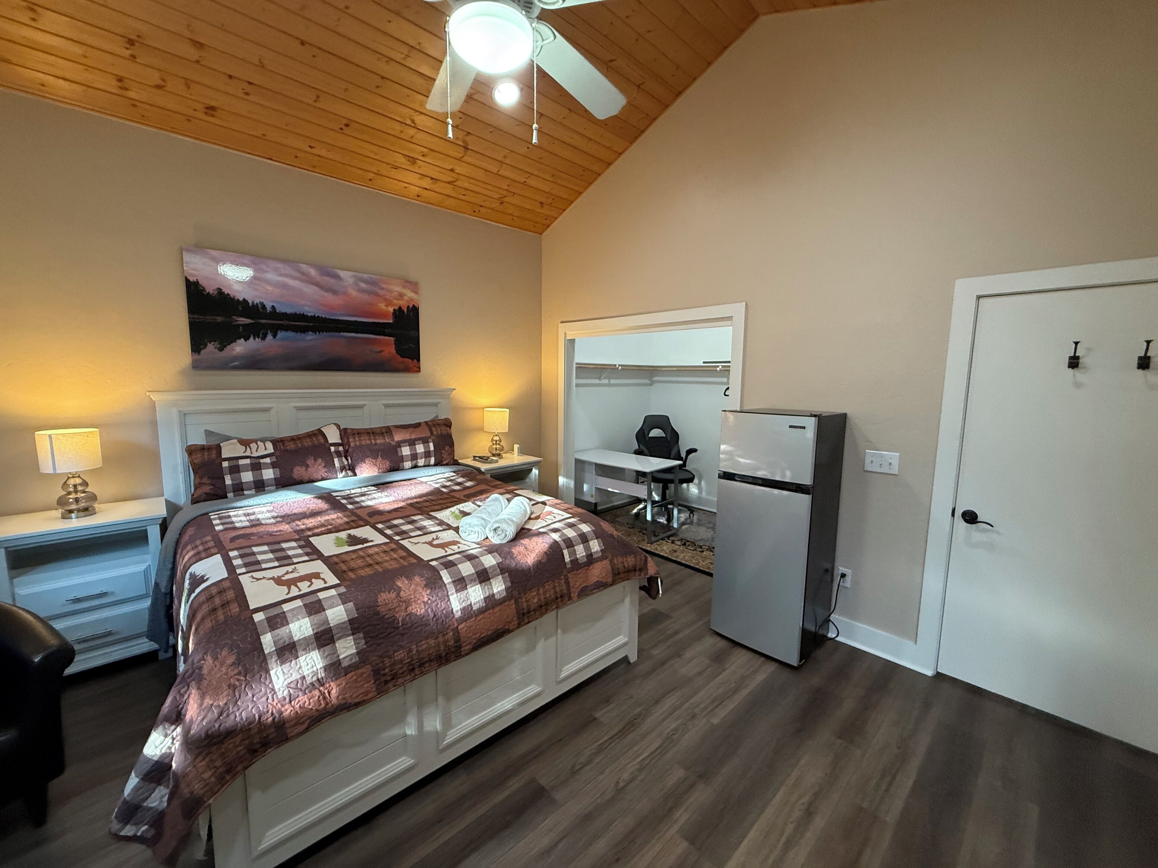 Une chambre avec un lit, un bureau, une chaise, un réfrigérateur et une porte.