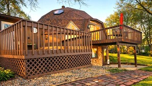 Ein hölzernes Pavillon mit geneigtem Dach, Steinunterbau und einer Holzterrasse mit Geländern.