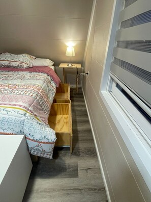 A narrow room with a bed, a small table with a lamp, and a window. - Cozy Shelter with Excellent Connectivity (Downtown and Airport) (Los Lagos)
