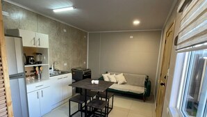 Cocina compacta con armarios blancos, una mesa de comedor con cuatro sillas y un sofá en la sala.
