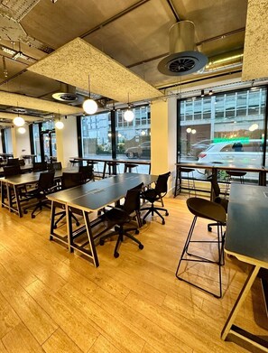 Een moderne vergaderzaal met grote tafels en stoelen, grote ramen en uitzicht op de straat.