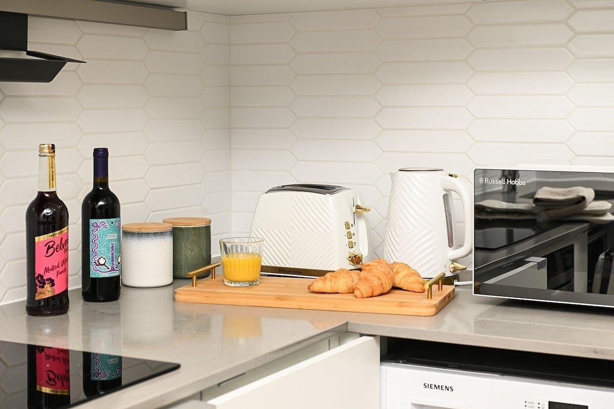 A kitchen counter with wine bottles, a toaster, a coffee maker, a glass of orange juice, and croissants.