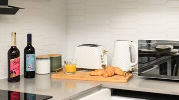 A kitchen counter with wine bottles, a toaster, a coffee maker, a glass of orange juice, and croissants.