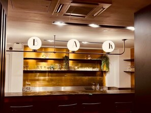 Een barruimte met verlichte letters 'B', 'A' en 'R' aan het plafond, planken met glazen en planten, en een modern ontwerp.