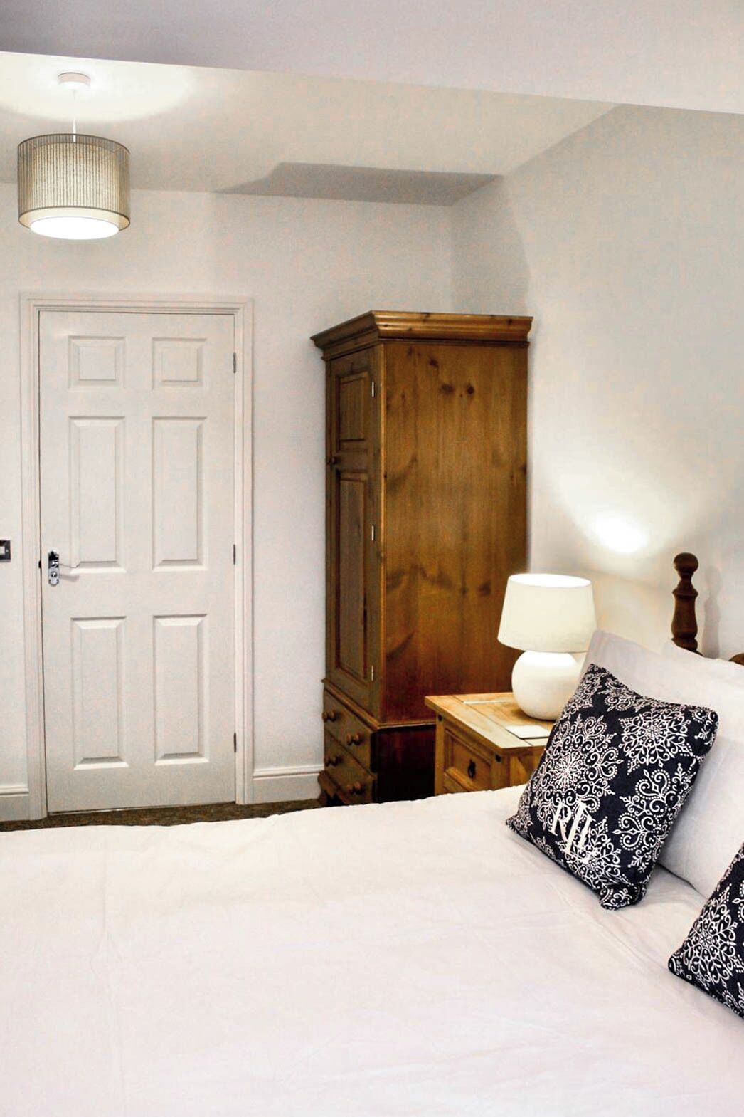 A bedroom with a bed, a wooden wardrobe, a nightstand with a lamp, and a white door.