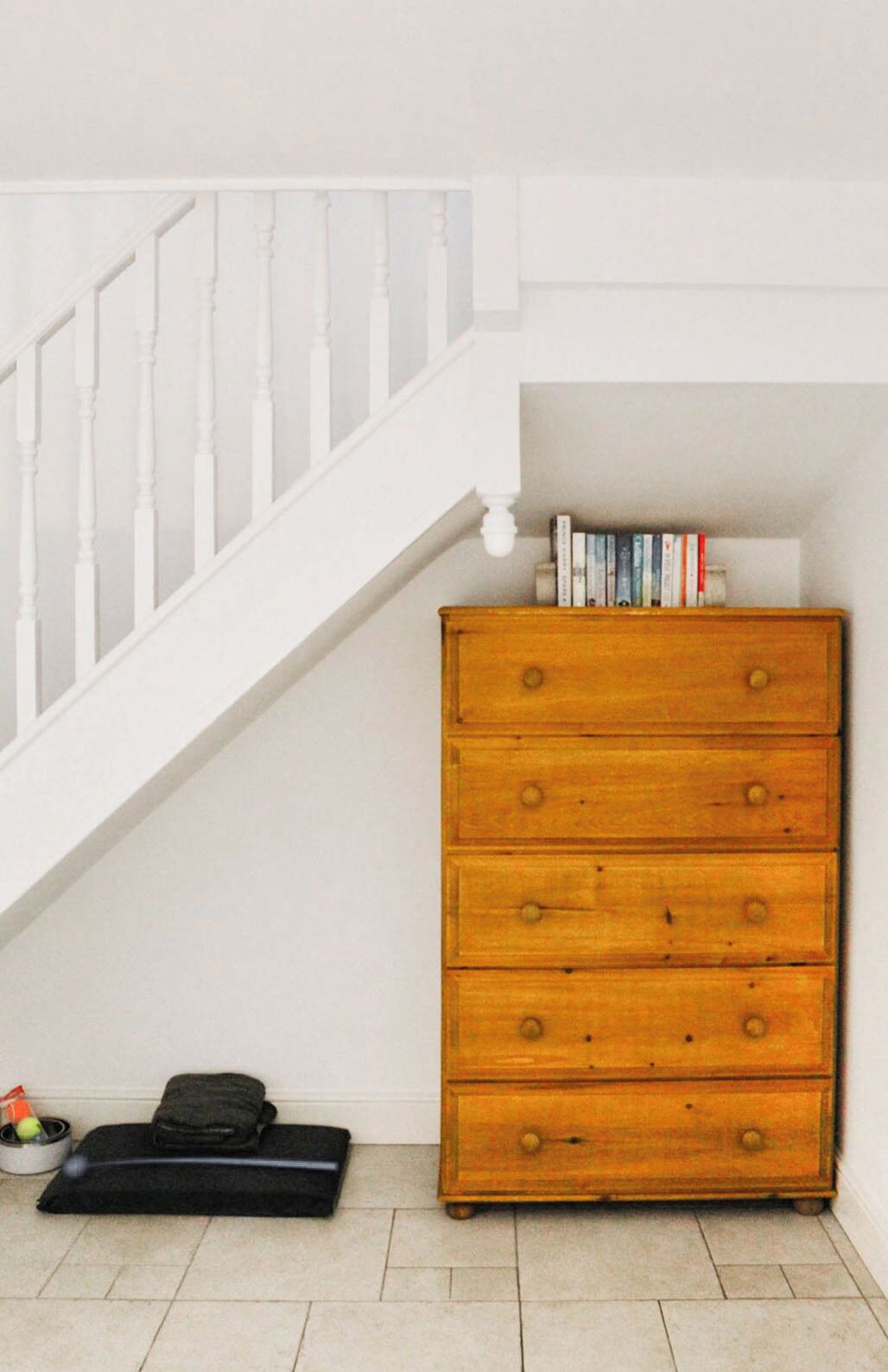 A staircase with white balusters, a wooden dresser with multiple drawers, and a small black pet bed with toys.