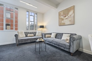 Ein Wohnzimmer mit zwei grauen Sofas, einem kleinen runden Tisch, einer Lampe und einem großen abstrakten Gemälde an der Wand.