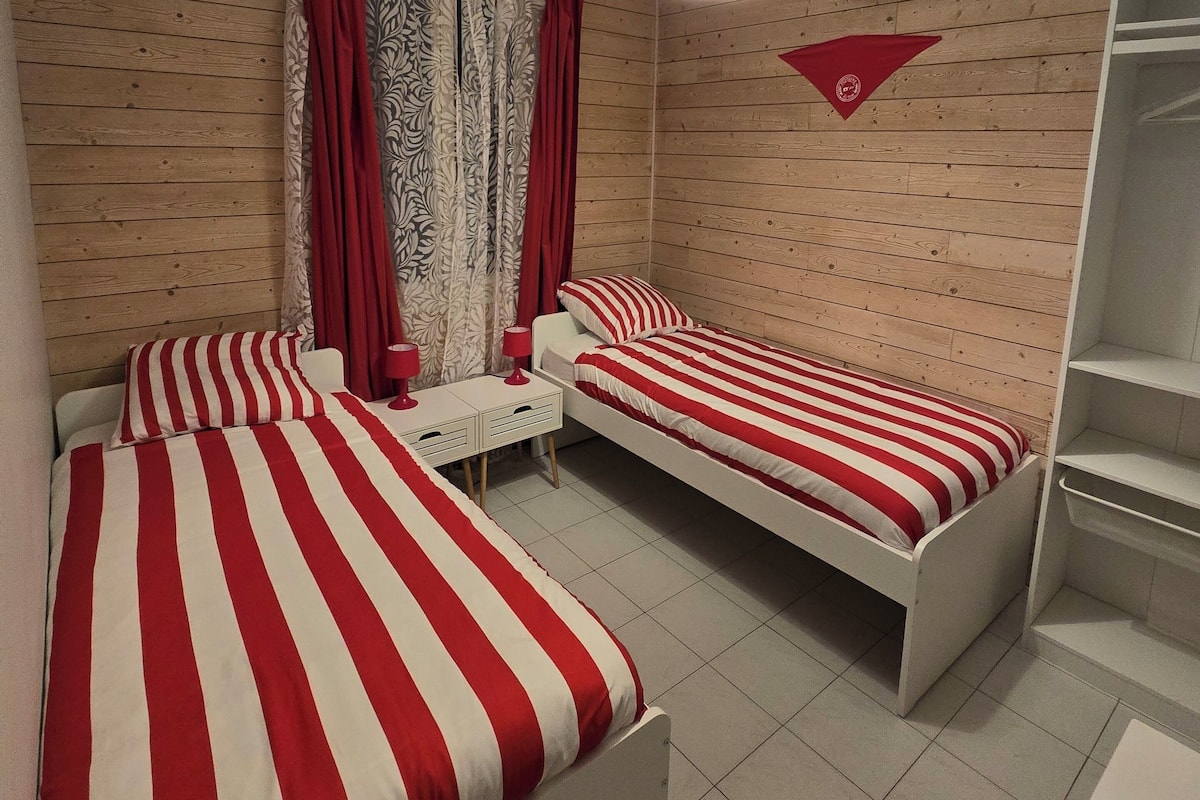 A room with two beds, a desk, a chair, a wardrobe, and a hanging light fixture.