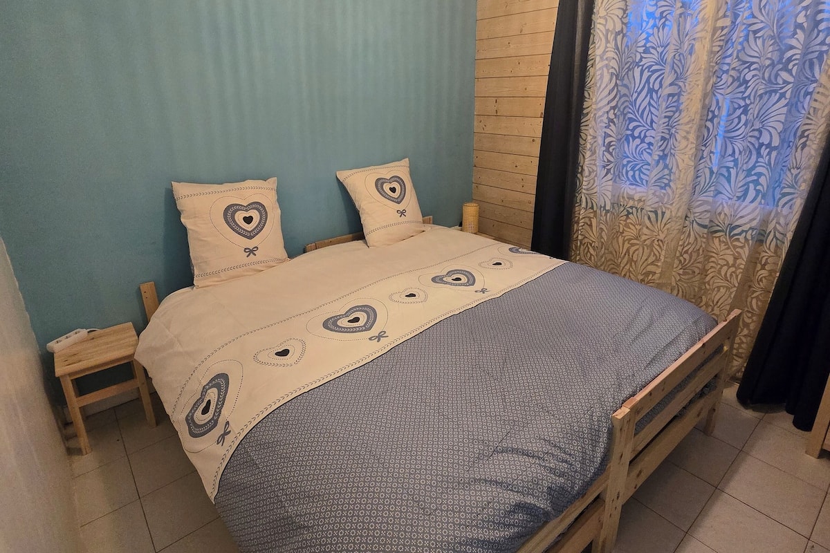 A bedroom with a wooden bed, a blue wall, and a patterned bedspread.
