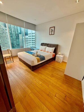 A modern bedroom with a large bed, a nightstand, a chair, and a view of tall buildings through large windows. - Vortex Suites Klcc By Bukit Bintang (Kuala Lumpur)