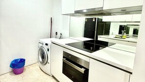 A modern kitchen with white cabinets, a built-in oven, a black induction cooktop, and a washing machine. - Vortex Suites Klcc By Bukit Bintang (Kuala Lumpur)