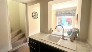 Una cocina con un lavamanos, un reloj y un ventanal con vistas al exterior.