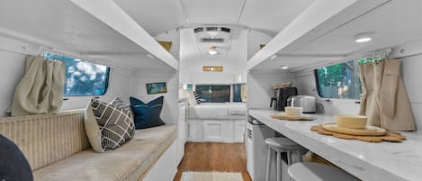 Interior compacto de una caravana con kitchenette, zona de estar y ventana.
