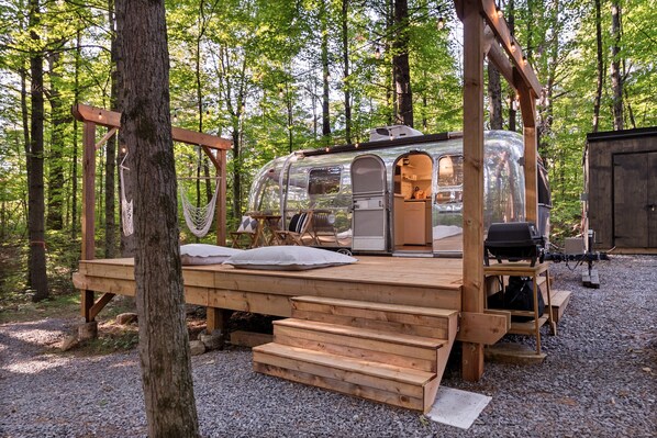 Un camping-car à parois transparentes doté d’une terrasse en bois, d’un hamac et d’un espace barbecue.