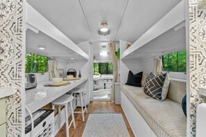 Un intérieur de camping-car compact comprenant un coin cuisine, un espace repas et un coin salon avec vue sur la verdure.