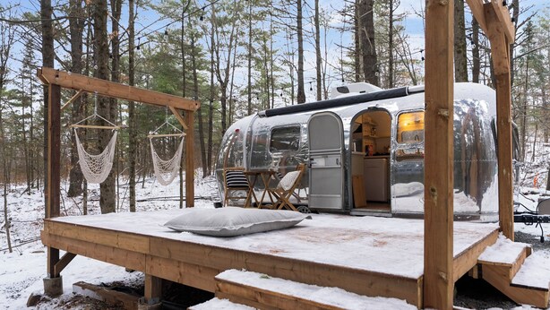 Una casa rodante con una terraza de madera y dos hamacas colgantes en un bosque nevado.