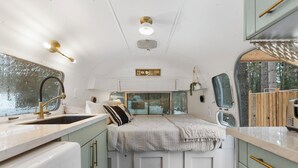 Cocina pequeña y bien iluminada con lavamanos, encimera y cama con manta a cuadros.
