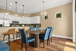 A modern kitchen with white cabinets, a dining table with blue chairs, and pendant lights. - Fully Renovated 5 BDR PCB House-Walk to Beach! (Panama City Beach)